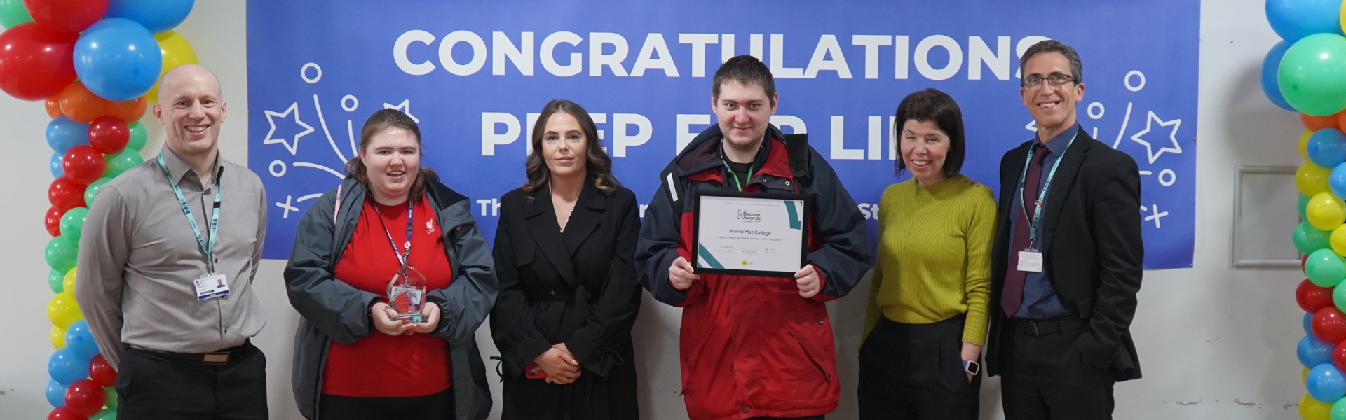 Wirral Met staff and students posing in front of congratulatory banner for Beacon Awards