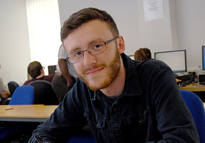 Wirral Met Accountancy student sitting in a classroom with computers behind him
