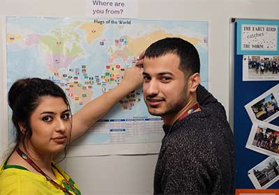 Two Wirral Met ESOL students standing and pointing at a map of the world