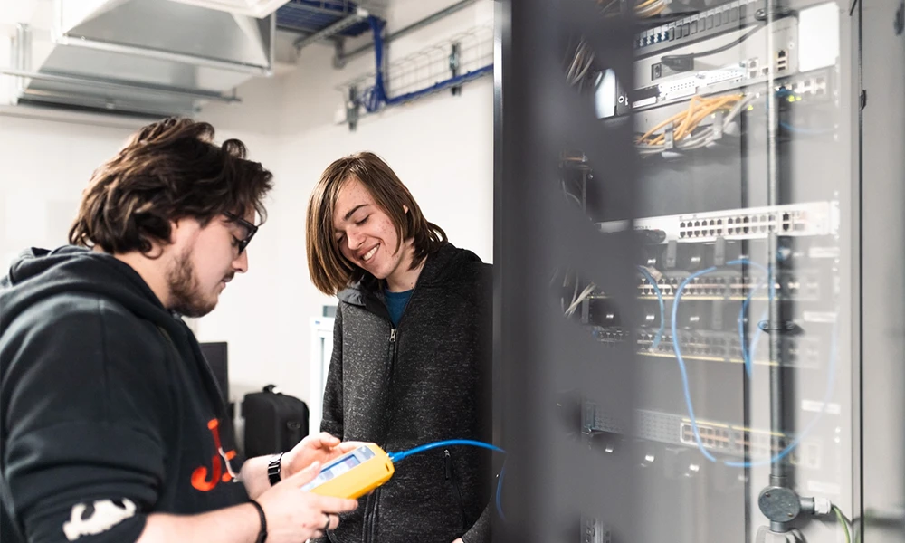 Two computing students working with wires inside server room