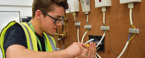 Apprentice electrician Michael Bayley, wearing glasses and high vis, installing wiring systems as part of his apprenticeship with Magenta Living