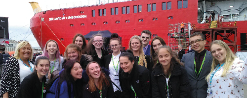 A group photo of Wirral Met College students and staff standing behind a red ship at the RRS Sir David Attenborough naming ceremony